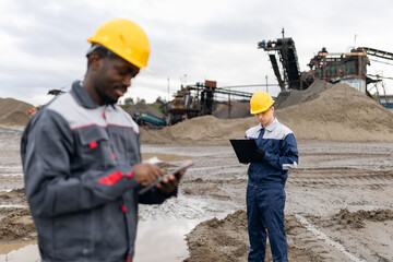 Engineers surveying sand quarry: african male and caucasian man in mining operations