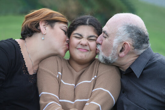 cheerful  family, mature latino couple kissing on a cheek  teenage girl with funny grimace  outdoors