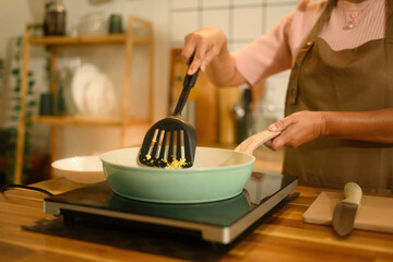 Close-up view of old woman hands stirring scrambled eggs in a non-stick pan on an electric stove