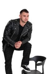 A handsome dark-haired man in a black leather jacket, black T-shirt, trousers and sneakers on a white background