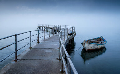 Obraz premium Serene Pier and Moored Boat on Calm Misty Water