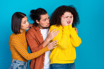 Three young friends comforting their upset companion against a blue studio background, showcasing...