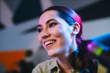 Young woman smiling under vibrant neon lights during an indoor studio podcast session