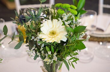 Romantic wedding centerpiece displaying white gerberas, green chrysanthemums, and eucalyptus leaves creating elegant floral arrangement