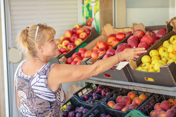 Mature woman choosing fruits in street shop in resort town. Summer healthy shopping in farm store