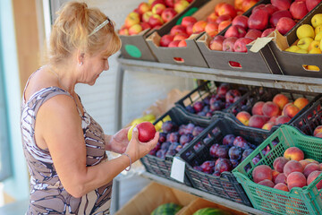 Mature woman choosing fruits in street shop in resort town. Summer healthy shopping in farm store
