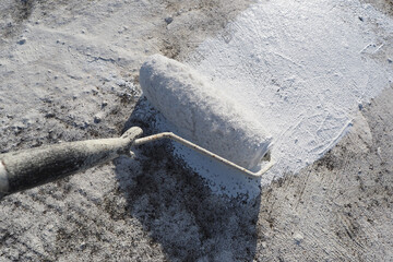 Painter applying a fresh white waterproof coat paint with a roller tool to a roof surface. POV.