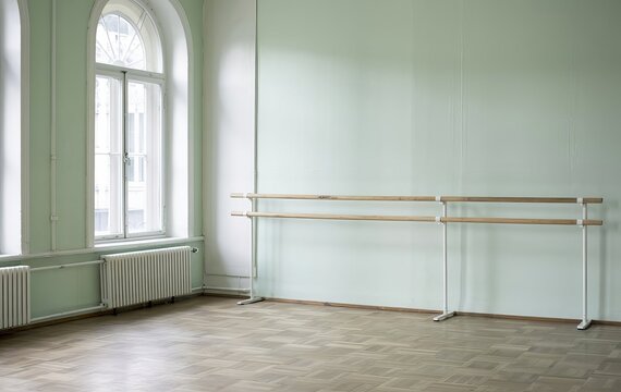 Empty ballet studio with wooden floor, large windows, and barre for practice