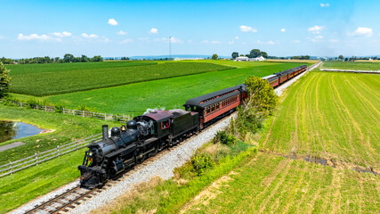 Vintage Steam Train Travels Through Lush Green Fields in Rural Landscape During Daytime. High quality photoA vintage steam train moves along a scenic track surrounded by vibrant green fields. Bright