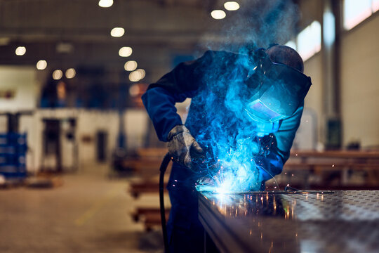 Welder Operating Equipment in Industrial Facility with Bright Sparks and Blue Light
