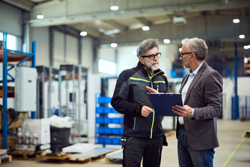 Two Professionals Discussing Work Within a Spacious Industrial Warehouse Setting