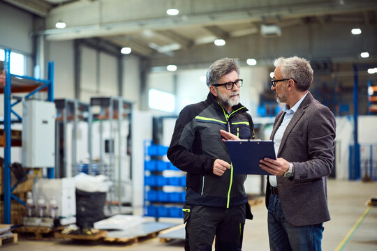 Two Professionals Discussing Work Within a Spacious Industrial Warehouse Setting - Powered by Adobe