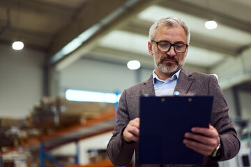 Senior Businessman Evaluating Documents in Modern Industrial Warehouse Setting
