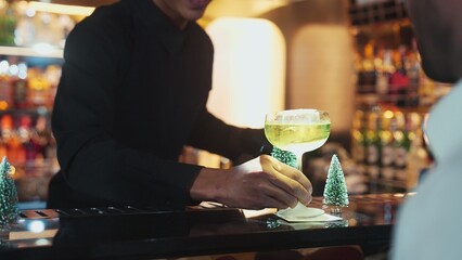 Special drink in Midori Sour cocktail with caramelized citrus slice and cinnamon power served stylish saucer glass by bartender serving to smart guest at luxurious bar christmas tree theme. Vinosity.