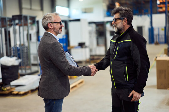 Two Professionals Shaking Hands in a Bright Industrial Factory Setting