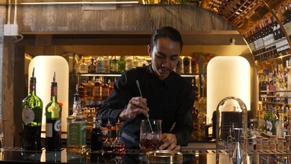 Smart Asian bartender using stirring mixed alcohol syrup into glass with ice for on the rock served mixing looking camera zoom out special refresh cocktail nightlife mixology at nightclub. Vinosity.