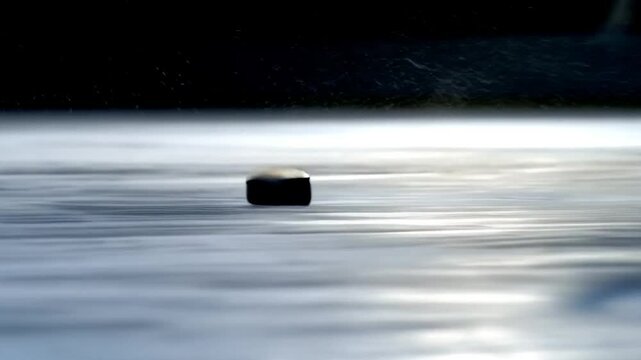 Dynamic shot of a hockey puck sliding on icy surface, splashing water droplets with a fast, energetic motion blur.