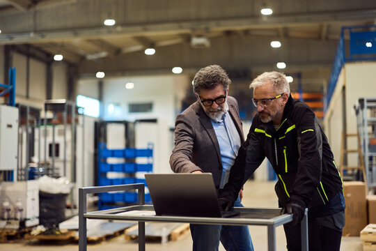 Two Professionals Discussing on a Laptop in a Modern Factory Floor