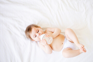 a baby falling asleep, a newborn girl in a diaper lies on a white crib in a bright bedroom and...