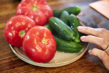 Close-up view of fresh washed tomatoes, cucumbers, and green onions arranged in a plate on a rustic wooden countertop. The image highlights healthy eating, fresh vegetables, and natural kitchen textur