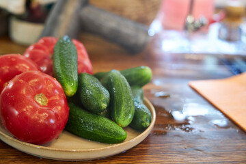 Close-up view of fresh washed tomatoes, cucumbers, and green onions arranged in a plate on a rustic wooden countertop. The image highlights healthy eating, fresh vegetables, and natural kitchen textur