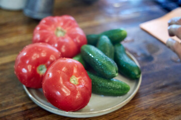 Close-up view of fresh washed tomatoes, cucumbers, and green onions arranged in a plate on a rustic wooden countertop. The image highlights healthy eating, fresh vegetables, and natural kitchen textur