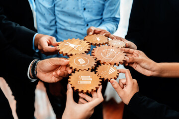 A diverse group of hands coming together to connect wooden gears, symbolizing collaboration and strategic planning in a modern business environment. Amity