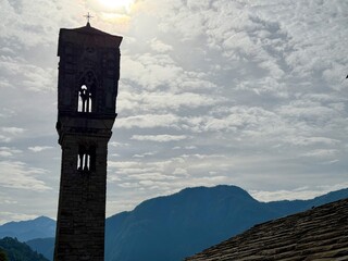 Bell tower of Santa Maria Maddalena in Ossuccio, Lake Como, Italy, featuring late Gothic belfry and Romanesque base, with scenic backdrop of lake and mountains on a serene summer day