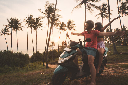 Romantic caucasian couple riders sit on rented scooter watch sunset in sri lanka . Freedom and adventure. Road trip. Embracing relationship togetherness and holidays in asia. Renting scooter concept - Powered by Adobe
