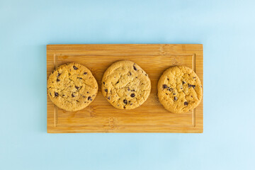 Three chocolate chip cookies on a wooden board
