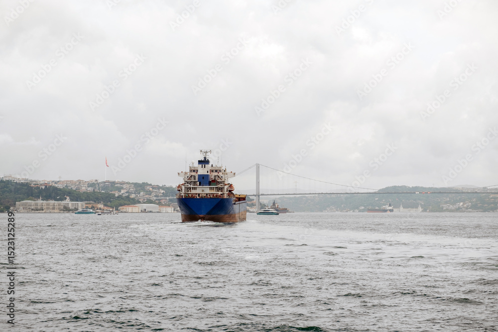 Poster Bosphorus Strait with cargo ship navigating under cloudy skies and bridge connecting Europe and Asia in the background
