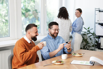 Man showing his colleague something on smartphone during lunch break in office