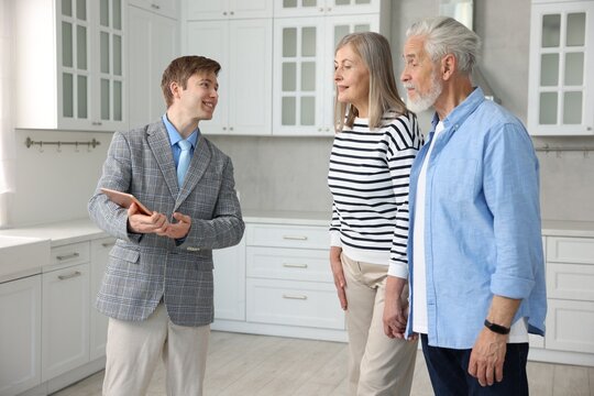 Smiling real estate agent with tablet working with couple in kitchen