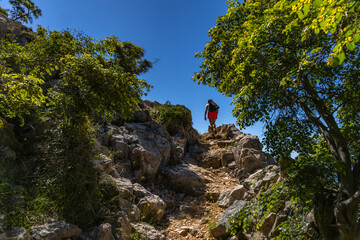 A woman in a white T-shirt and pink skirt walks along a hiking trail leading through the mountains...