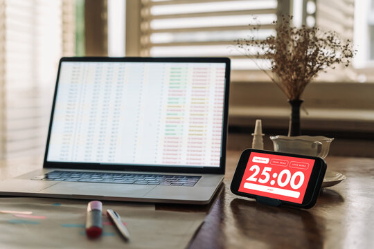 Work from home productivity setup featuring a Pomodoro timer app, paper planner, laptop and smartphone. Time management and work-life balance