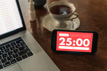 Work from home productivity setup featuring a Pomodoro timer app, paper planner, laptop and smartphone. Time management and work-life balance