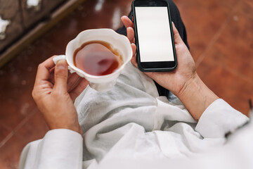 Smartphone with blank screen held by woman on balcony, suitable for app design mockups or digital lifestyle visuals. Peaceful outdoor moment