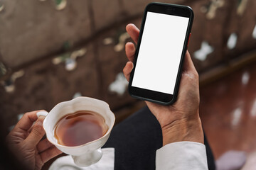Smartphone with blank screen held by woman on balcony, suitable for app design mockups or digital lifestyle visuals. Peaceful outdoor moment