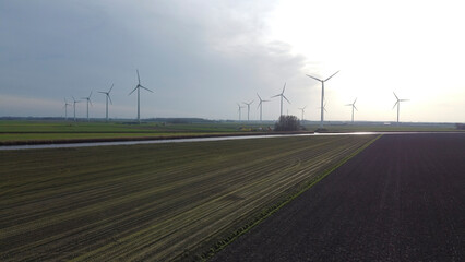 Wind turbines harnessing renewable energy across a vast farmland landscape under a cloudy sky