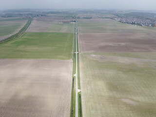 Expansive agricultural landscape with fields, pathways, and distant towns under a cloudy sky during...