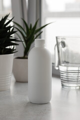 A white bottle with medicinal aloe juice on the background of an aloe flower and a carafe of water....