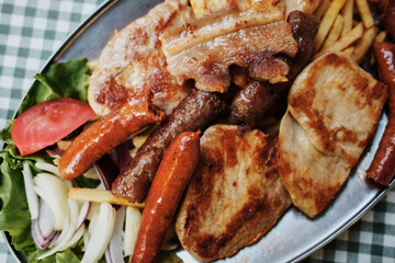 Close-up of a traditional Serbian grilled meat platter with sausages, pork and French fries served on a metal plate. Balkan cuisine.