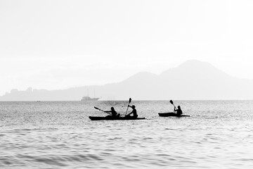 Three athletes paddling their kayaks on a cloudy day