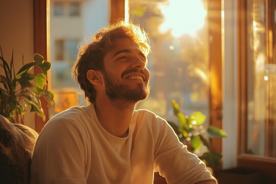 Smiling Young Man Indoors at Sunset. Capturing Natural Light and Relaxation in a Carefree Portrait