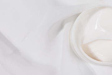Minimalist skincare scene featuring a white whitening cream container elegantly placed on soft white satin, symbolizing purity and luxury.