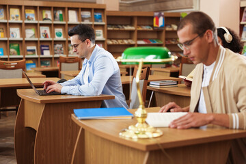 People studying at desks in public library, selective focus