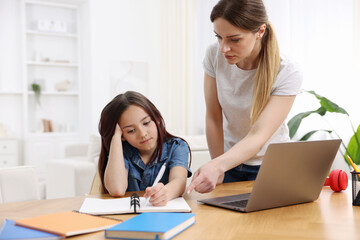 Mother helping her daughter with homework at wooden table indoors
