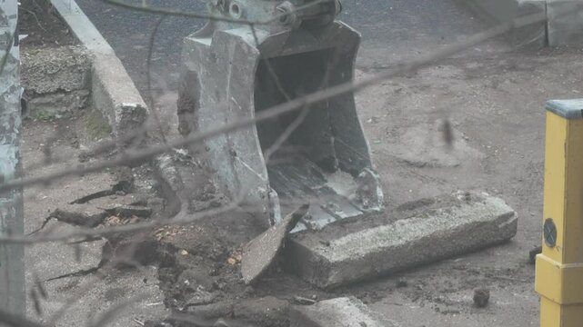 Excavator Roadwork Concrete: Excavator removes concrete blocks during road repair in city street, daytime.