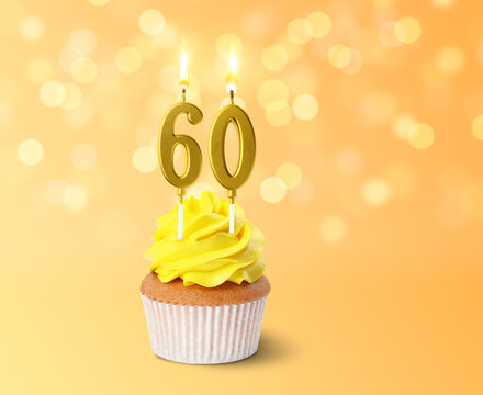 Yummy cupcake with burning number shaped candles on color gradient background with blurred lights. 60th birthday or other special occasion