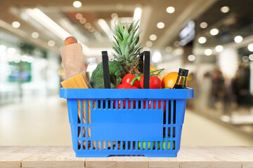 Blue shopping basket full of groceries on wooden table in supermarket